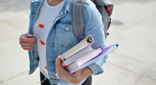 Woman wearing denim jacket and backpack, holding books and folders