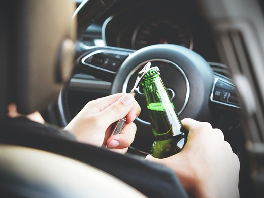 Image of someone opening a beer in the drivers seat of a car