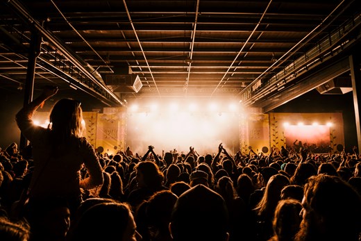 Image of a concert stage showing a large crowed of people in front of them listening to music.